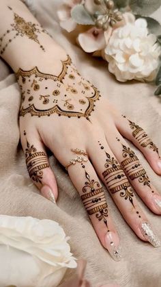 a woman's hand with henna tattoos on it and flowers in the background