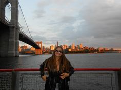 a woman standing in front of a bridge with the city skyline in the back ground