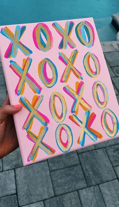 a person holding up a pink box with letters painted on it in front of a swimming pool