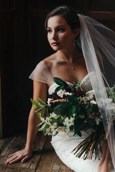 a bride sitting on the floor with her bouquet in hand and veil over her head