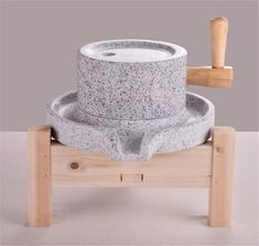 a stone water fountain with wooden stand and hammer on the top, in front of a gray background