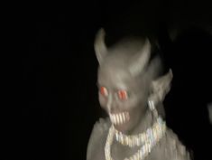 a creepy creature with red eyes and silver necklace in the dark, looking at camera