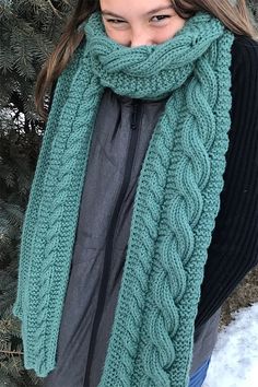 a woman standing in front of a tree wearing a green knitted scarf and hat