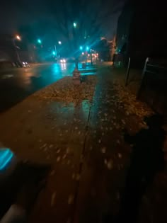 an empty street at night with the lights on and fallen leaves covering the ground in front of it