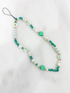 a white and green beaded necklace on a marble surface with an evil eye charm