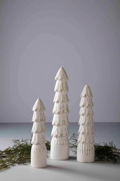 three white ceramic trees sitting on top of a snow covered ground in front of a gray sky