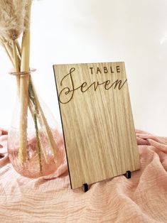 a wooden table sign sitting next to a vase with dried flowers