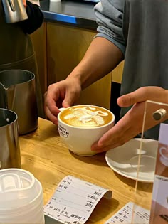 a person holding a cup of coffee on top of a wooden table next to cups and saucers