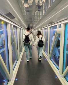 two people walking down a long hallway with glass walls on both sides and one person carrying a backpack