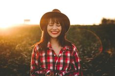 a woman in a plaid shirt and hat smiles at the camera with her eyes closed