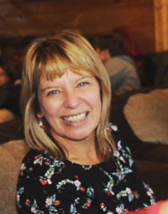 a woman sitting on a couch smiling at the camera with people in the room behind her