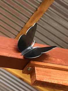 a metal butterfly sitting on top of a wooden table next to a piece of wood