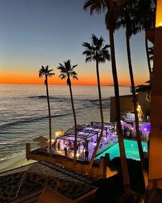 an aerial view of the beach and ocean at sunset with palm trees in foreground