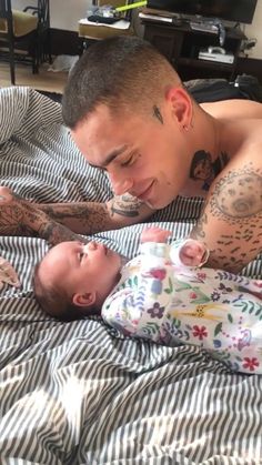 a man with tattoos on his arms and chest laying next to a baby