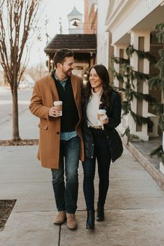 a man and woman are walking down the sidewalk together holding coffee cups in their hands