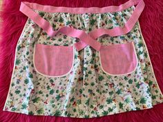 a pink and white flowered skirt with two pockets on the front, sitting on a pink furnishing