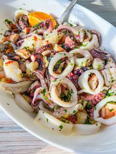 an octopus salad is served in a white bowl on a wooden table with a fork