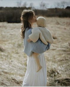 a woman holding a child in her arms while standing in a field with dry grass