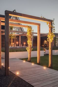 a wooden walkway with lit up plants on each side and an outdoor dining area in the background