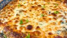 a cheesy dish with cheese and green onions in a blue casserole dish