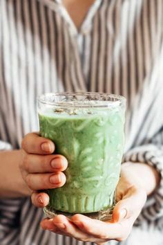 a woman holding a green smoothie in her hands