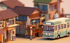 a toy bus is parked in front of some small model houses and stores on the street