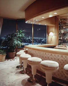 a bar with four stools in front of it and a view of the city at night