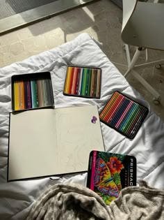 there are many different colored pencils on the bed and one has a drawing book