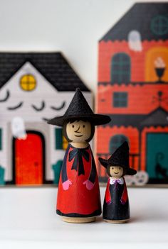 two wooden dolls are standing next to each other in front of a house and dollhouse