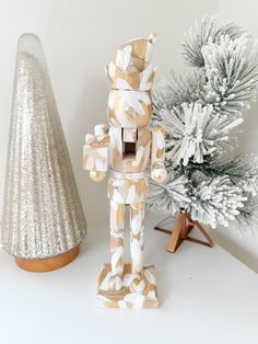 a wooden toy standing next to a small christmas tree on a white table with silver decorations