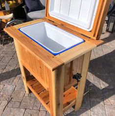 an open wooden cooler sitting on top of a brick floor next to a table and chairs