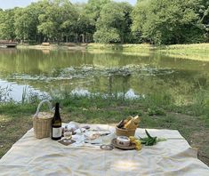 a picnic table with food and wine on it next to a lake in the woods