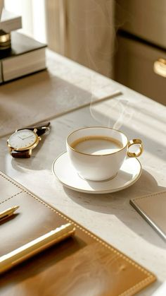 a cup of coffee sitting on top of a saucer next to a notebook and watch