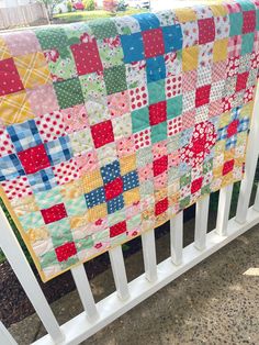 a multicolored patchwork quilt hanging on a white fence