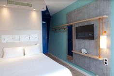 a bedroom with blue walls and white bedding, tv mounted on the wall next to it