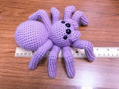 a purple stuffed animal sitting on top of a wooden table next to a measuring tape