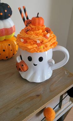 a white cup filled with candy and pumpkins on top of a wooden table next to other decorations