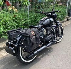 a black motorcycle parked on the side of the road next to some bushes and trees