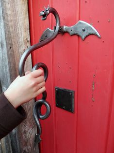 a hand is holding the handle to a red door with black metal hardware on it