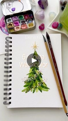 a christmas tree is shown on the cover of a notebook with watercolor paints and pencils