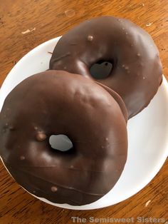 two chocolate covered donuts sitting on top of a white plate