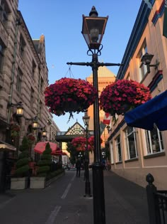 a street light with flowers hanging from it's sides and buildings in the background