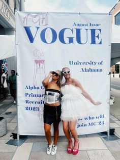 two women standing next to each other in front of a sign