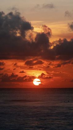 the sun is setting over the ocean with clouds