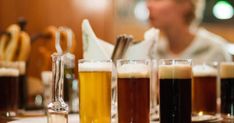 there are many different types of beer in the glasses on the bar counter, and one person is sitting behind them