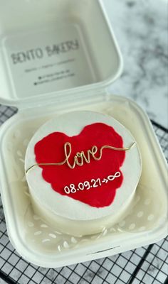 a heart shaped cake with the word love on it sitting in a plastic container next to a tray