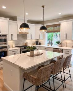 a large kitchen with white cabinets and marble counter tops, two pendant lights over the island