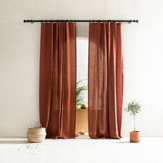 an open window with red curtains and potted plants on the floor next to it