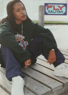 a woman sitting on top of a wooden bench next to a sign that says fly aaliyah