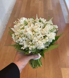 a hand holding a bouquet of white flowers on a wooden floor in front of a door